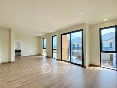 Spacious modern living room with large windows and balcony access, featuring elegant wooden flooring.