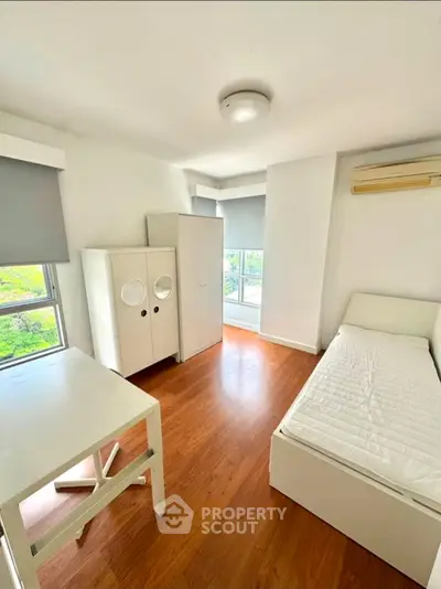 Bright minimalist bedroom with large windows and wooden flooring, featuring a single bed and modern furniture.