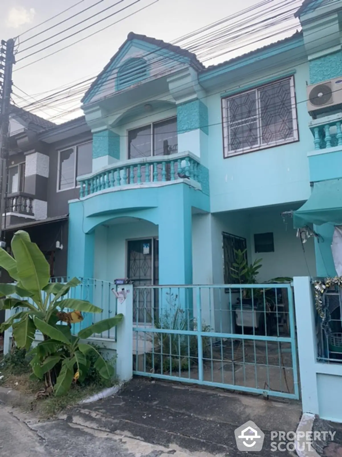 Charming turquoise townhouse with gated entrance and balcony in a serene neighborhood.