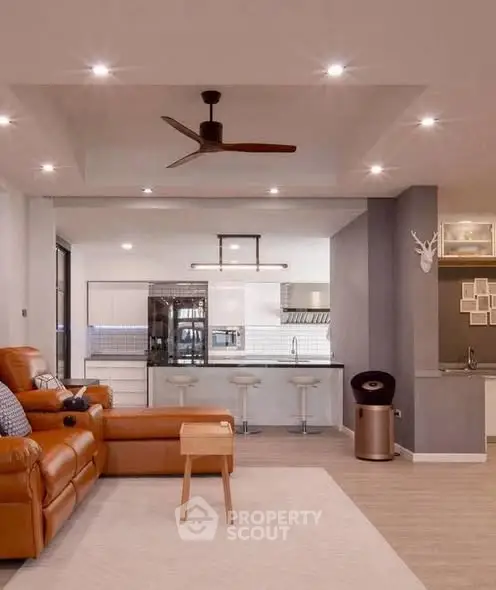 Modern open-plan living room with stylish kitchen and leather seating, featuring contemporary lighting and decor.