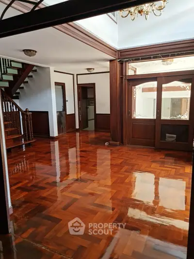 Spacious wooden-floored living room with elegant staircase and large windows.
