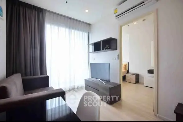Modern living room with sleek furniture and natural light, open doorway to bedroom.