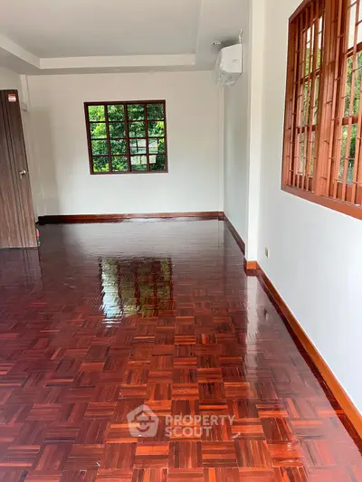 Spacious room with polished wooden floors and large windows offering natural light.