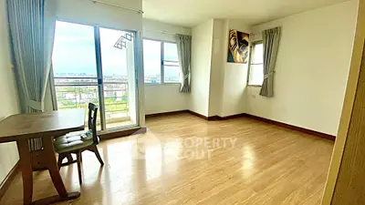 Spacious living room with balcony and city view, featuring wooden flooring and natural light.