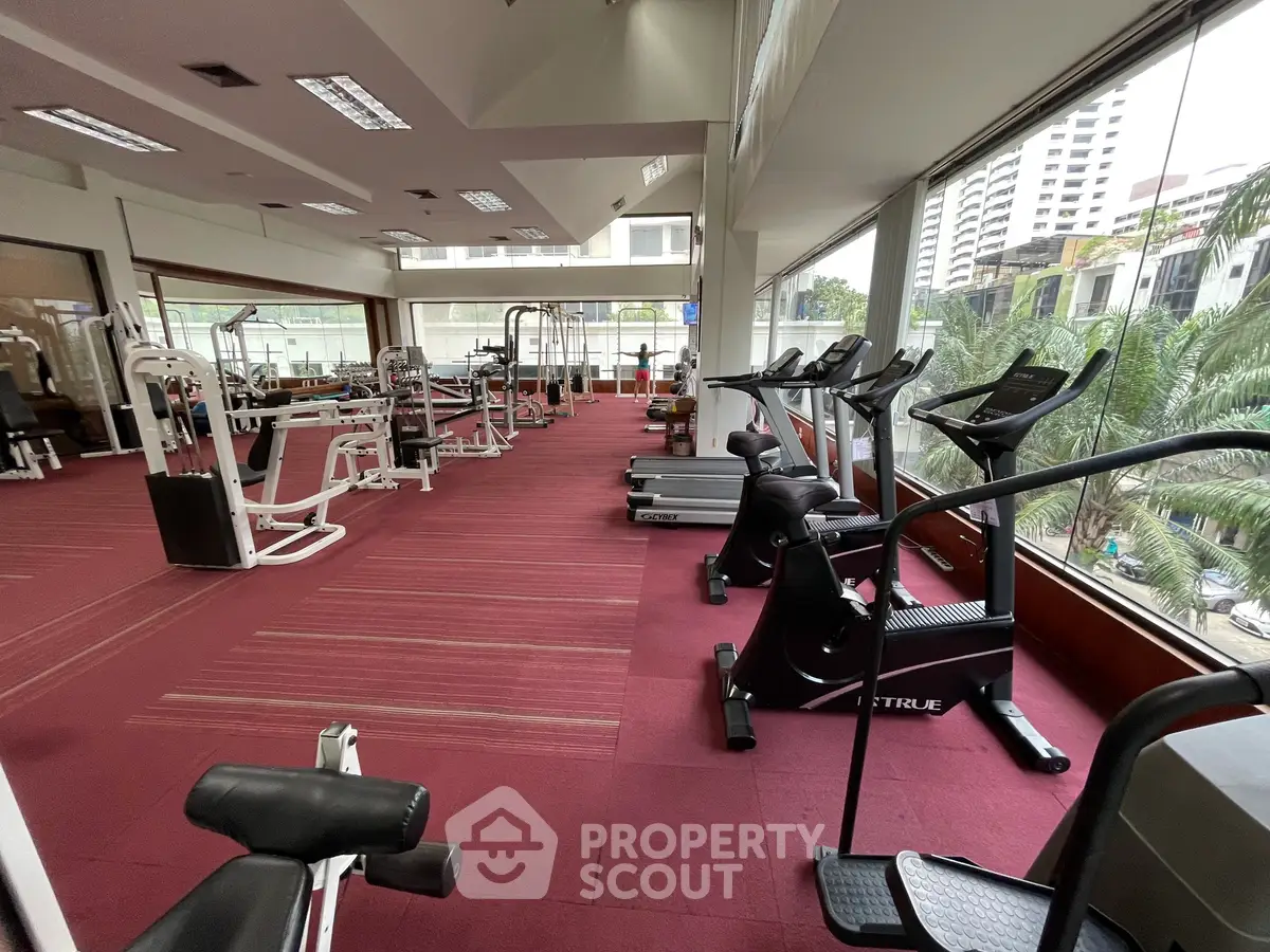 Spacious gym with modern equipment and large windows offering city views.