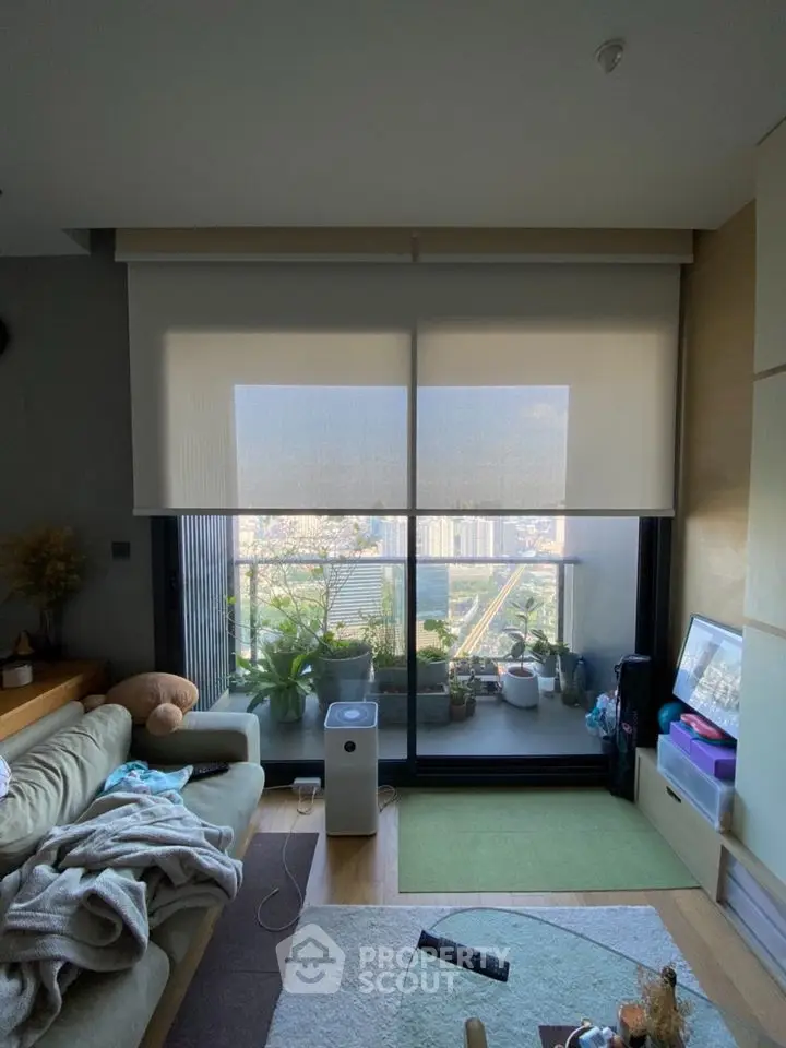 Modern living room with large balcony and city view, featuring cozy seating and indoor plants.