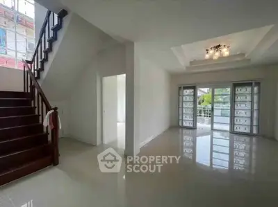 Spacious living room with elegant staircase and large windows offering natural light.