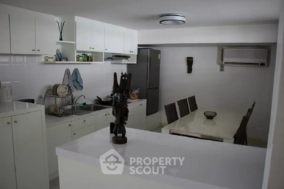 Modern kitchen with dining area, featuring sleek white cabinetry and stainless steel appliances.