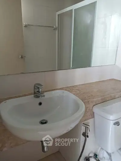 Modern bathroom with sleek sink and toilet, featuring a glass shower door and neutral tones.