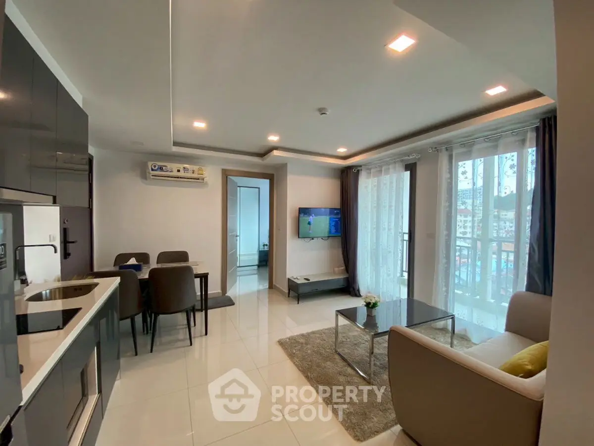 Modern living room with open kitchen and balcony view, sleek furniture and bright lighting.