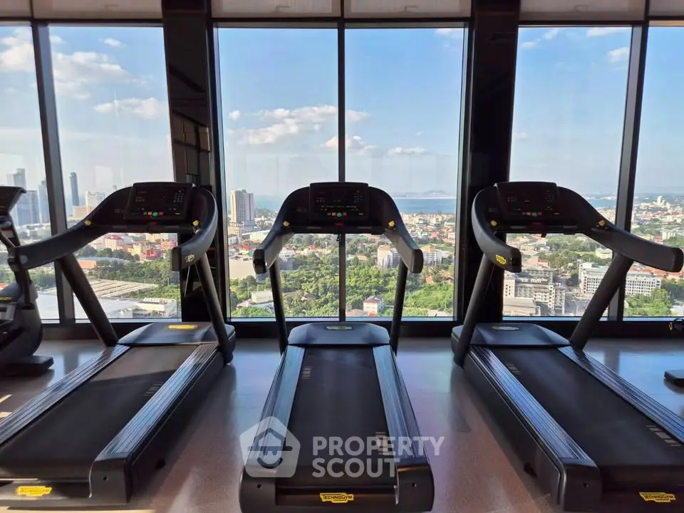 Luxury gym with panoramic city views and modern treadmills in high-rise building.
