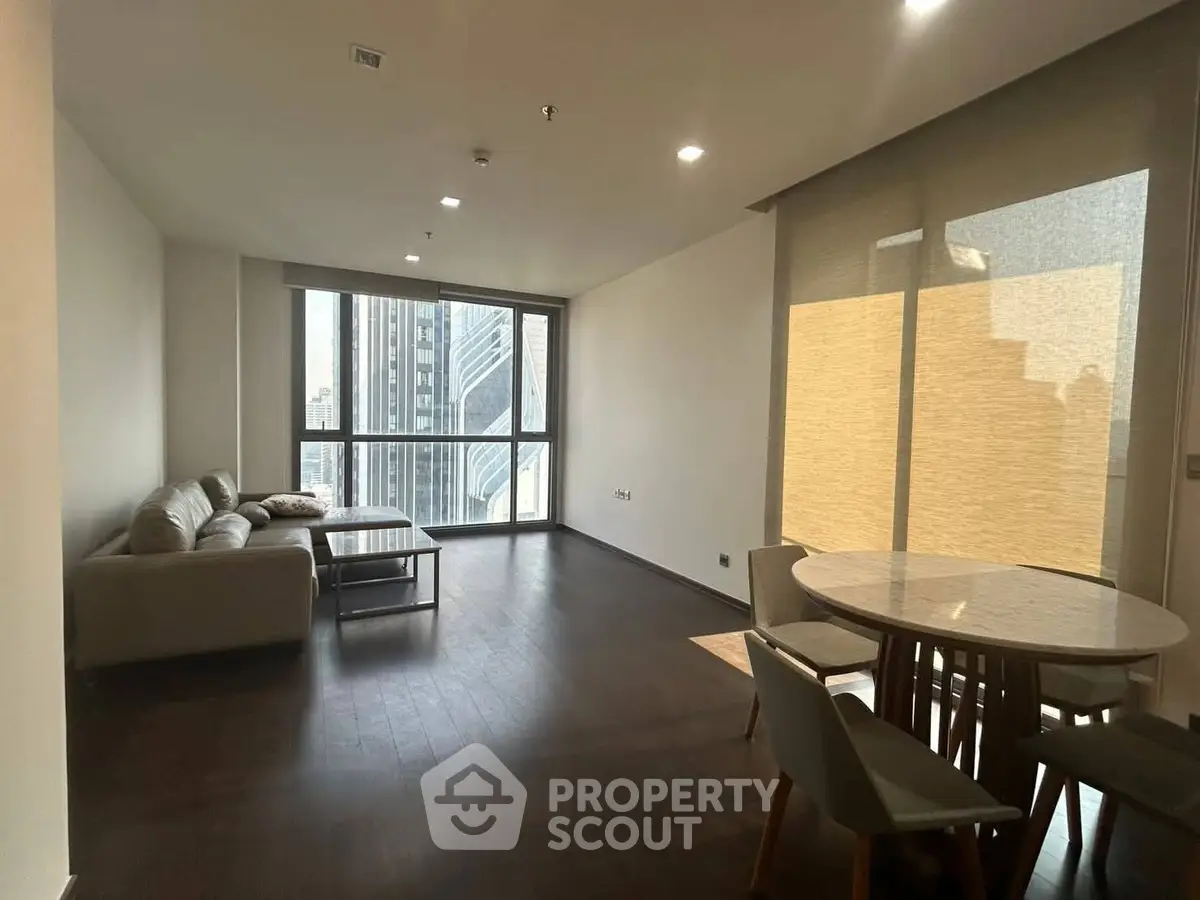 Spacious modern living room with city view, featuring elegant furniture and large windows.