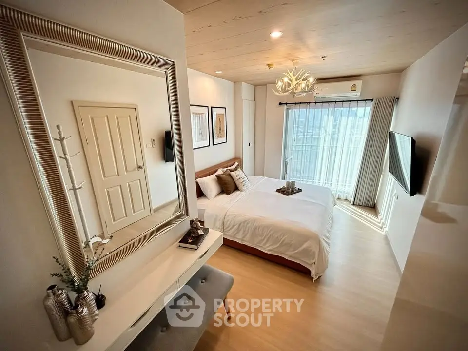Spacious modern bedroom with elegant decor and large mirror, featuring natural light and stylish furnishings.
