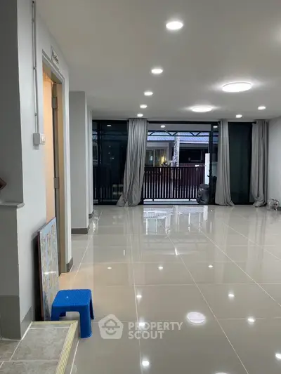 Spacious modern living room with glossy tiled floors and large windows opening to a balcony.