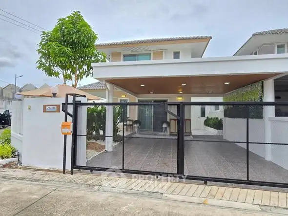 Modern two-story house with gated entrance and carport in a suburban neighborhood.
