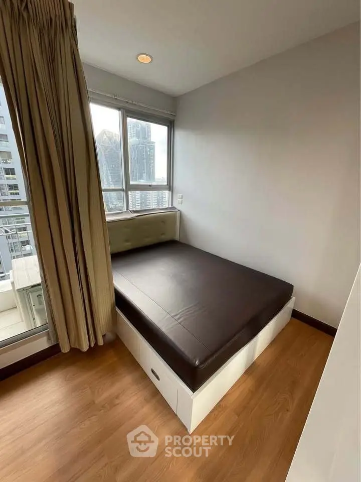 Cozy bedroom with city view, featuring a compact bed and large windows for natural light.