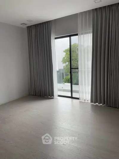 Spacious empty room with large window and elegant curtains, offering a serene view of greenery.