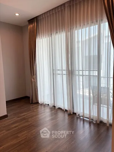 Spacious room with elegant floor-to-ceiling curtains and wooden flooring, perfect for modern living.