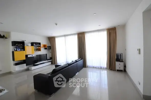 Spacious modern living room with sleek black sofa and large windows for natural light.