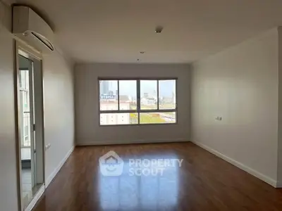 Spacious empty living room with large window and wooden flooring in modern apartment.