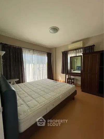 Spacious bedroom with natural light, featuring a large bed, wardrobe, and vanity desk.