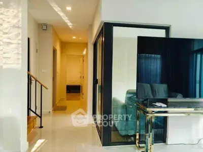 Modern living room with sleek design and large TV, featuring glass doors and bright lighting.
