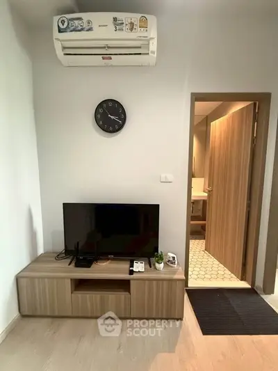 Modern living room with air conditioning and TV, featuring a sleek wooden cabinet and open bathroom door.