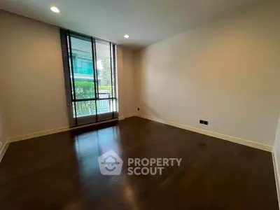 Spacious empty room with dark wood flooring and large window, perfect for customization.