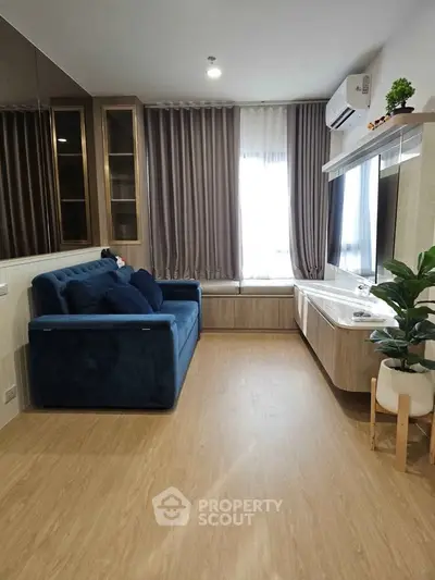 Modern living room with stylish blue sofa, large window, and sleek wooden flooring.