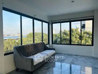 Spacious living room with large windows offering a stunning view of greenery.