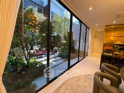 Luxurious living room with floor-to-ceiling windows overlooking a lush garden, featuring elegant decor and ample natural light.