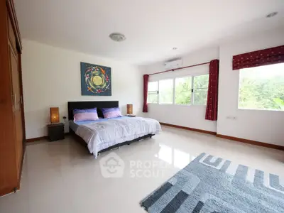 Spacious bedroom with large windows and modern decor in a serene setting.