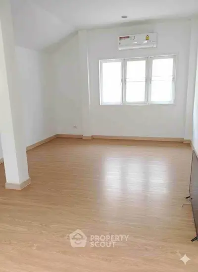 Spacious empty room with wooden flooring and large windows, perfect for customization.
