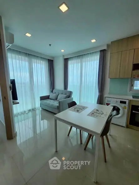 Modern living room with large windows, cozy sofa, and dining area in open layout apartment.