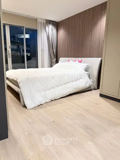 Modern bedroom with elegant wooden flooring and cozy bed near large window.