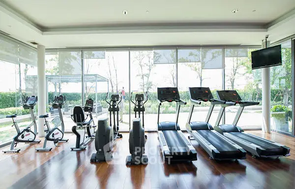 Spacious gym with modern equipment and large windows offering garden views.