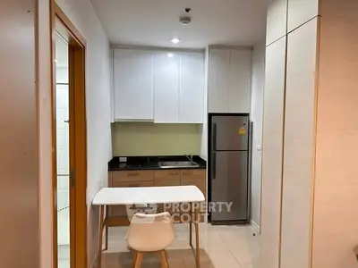 Compact modern kitchen with sleek cabinets and dining area in cozy apartment.