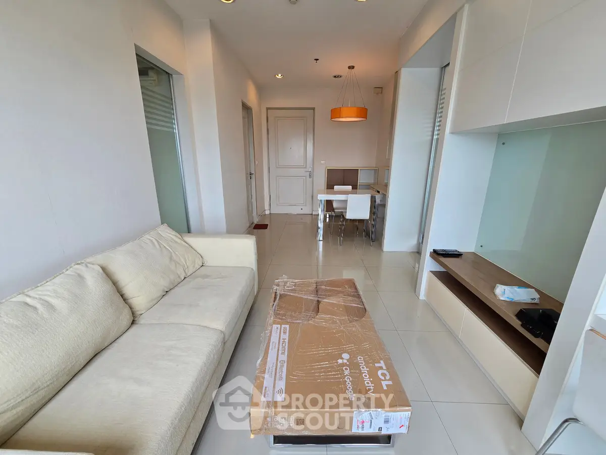 Modern living room with beige sofa and dining area in open layout apartment.