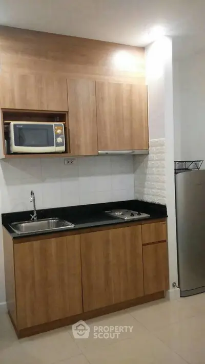 Modern compact kitchen with wooden cabinets and built-in microwave, ideal for urban living.