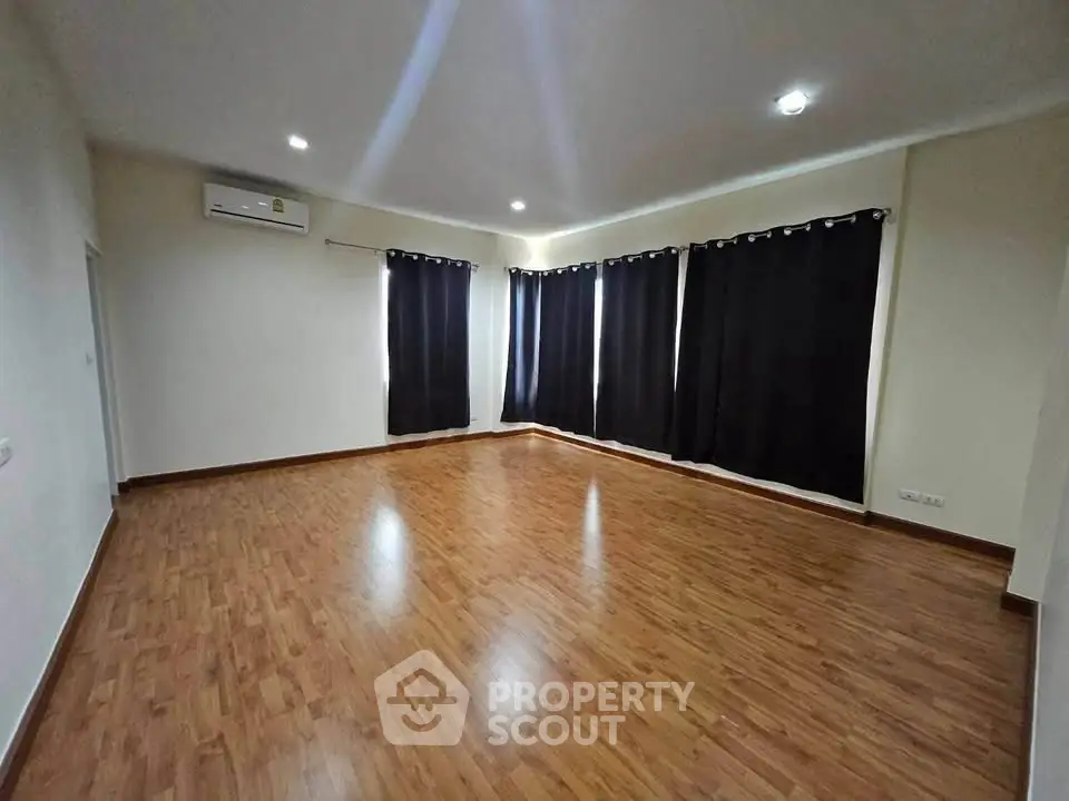 Spacious empty room with wooden flooring and large windows, ideal for customization.