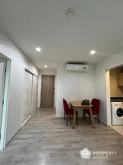 Modern apartment interior with dining area and washing machine, featuring sleek flooring and bright lighting.