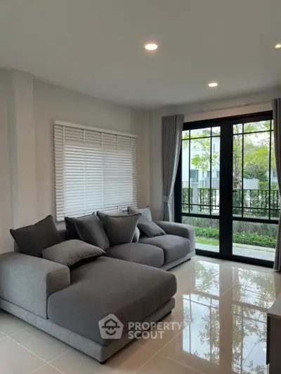 Modern living room with large windows and stylish gray sofas overlooking a lush garden.