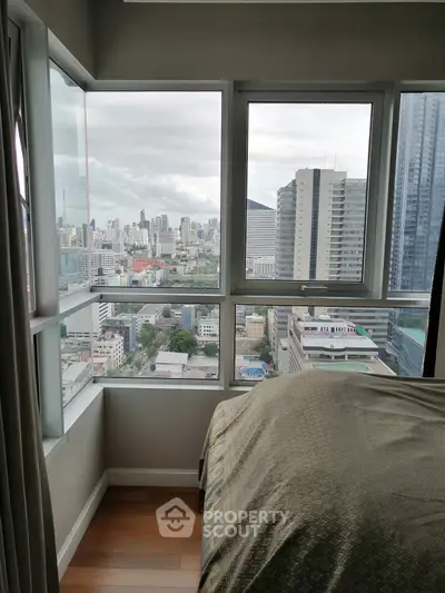 Stunning city view from a high-rise bedroom with large windows, offering a panoramic urban skyline.