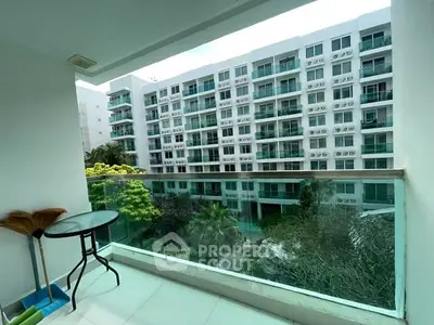 Spacious balcony with glass railing overlooking modern apartment complex and lush greenery.