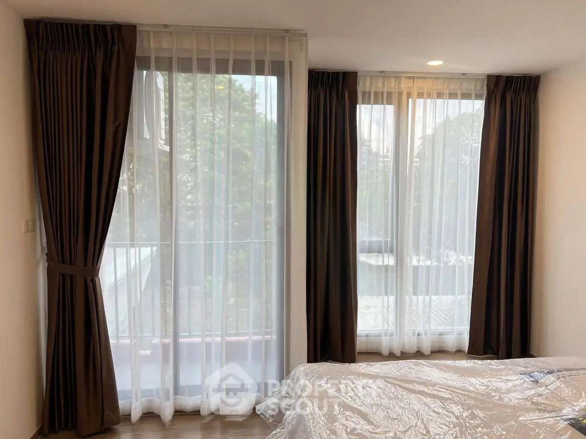 Spacious bedroom with large windows and elegant curtains offering a serene view.