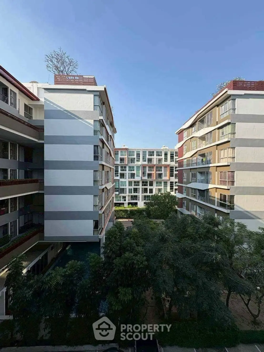 Modern residential apartment buildings with lush greenery and clear blue sky.