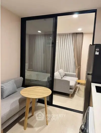 Modern apartment with cozy living area and glass partition, featuring stylish furniture and natural light.
