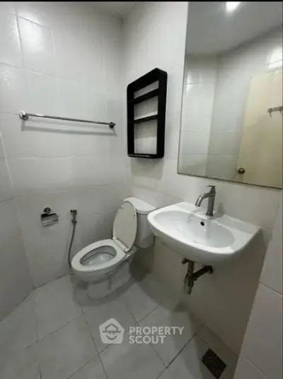 Compact bathroom with white tiles, toilet, sink, and wall shelf.