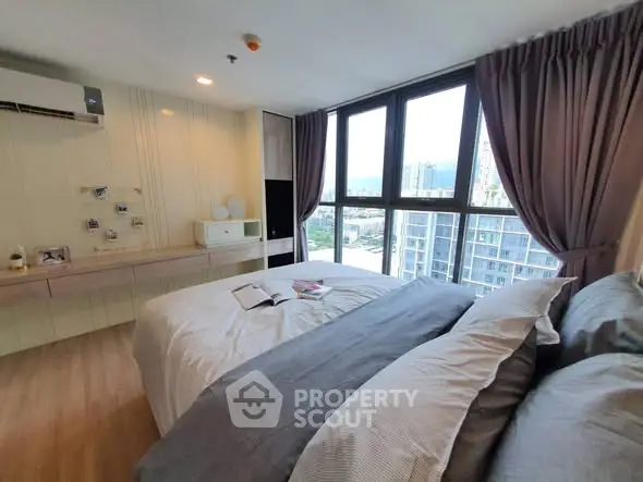 Spacious bedroom with large windows offering stunning city views, modern decor, and ample natural light.