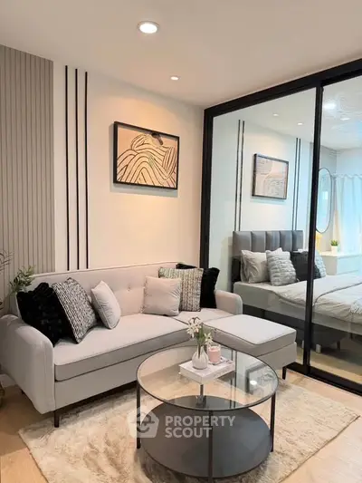 Modern living room with stylish decor and glass partition leading to a cozy bedroom.